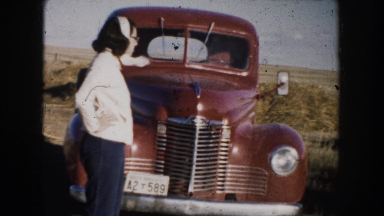 Woman in light jacket stands beside a red truck in an open field.