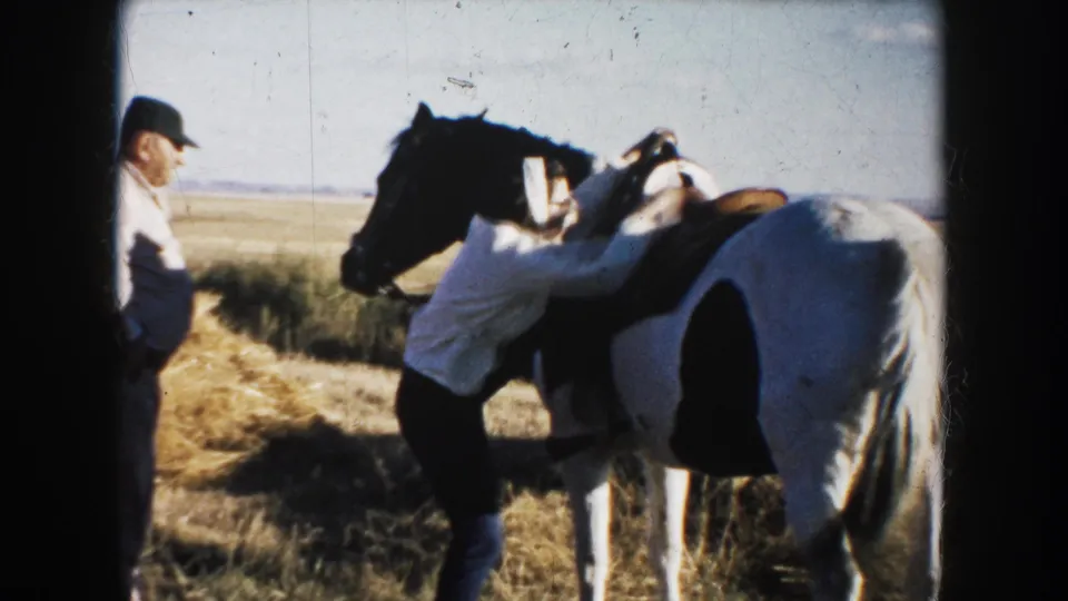 In a 1953 South Dakota field, a woman leans over a saddled pinto horse while a man stands to the side.