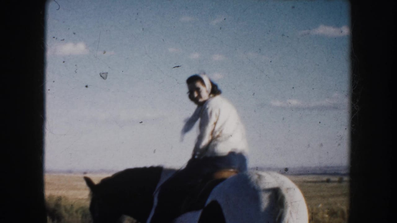 Woman rides a black-and-white horse across an open field under a blue sky.