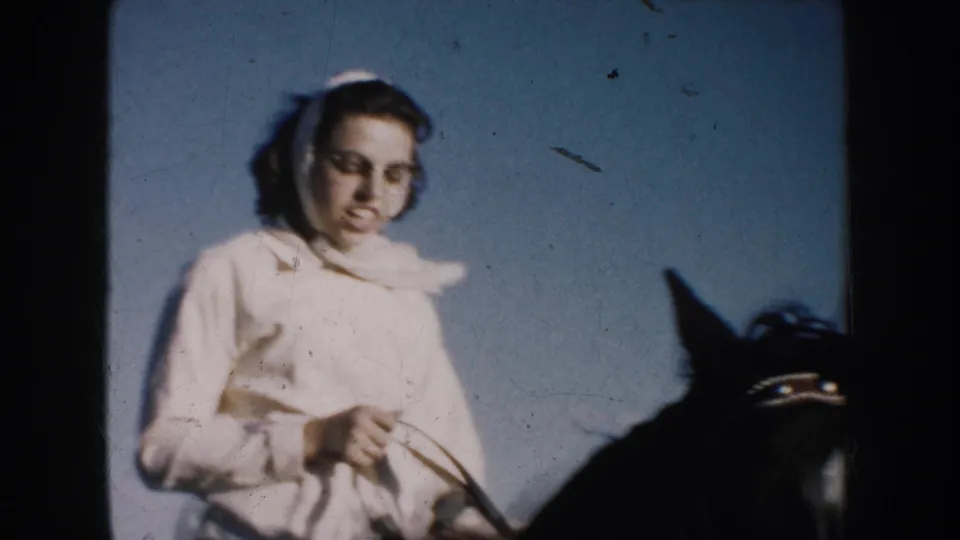 Close 1953 South Dakota home-movie view of a woman in a headscarf near a horse, appearing to talk while holding the reins.