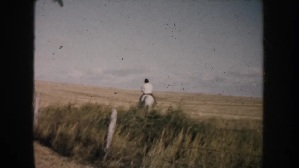 In 1953 South Dakota home-movie footage, a woman rides a horse away across open prairie near a simple fence line.