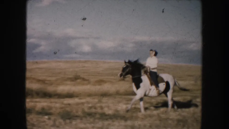 A woman in a light top rides a black-and-white horse across the South Dakota prairie in a closer side view.