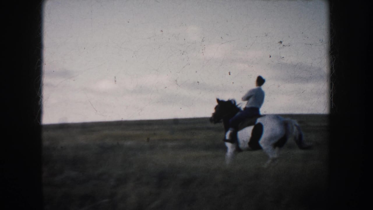 In South Dakota, 1953, a rider in light clothing sits on a black-and-white pinto horse in an open grassy field.
