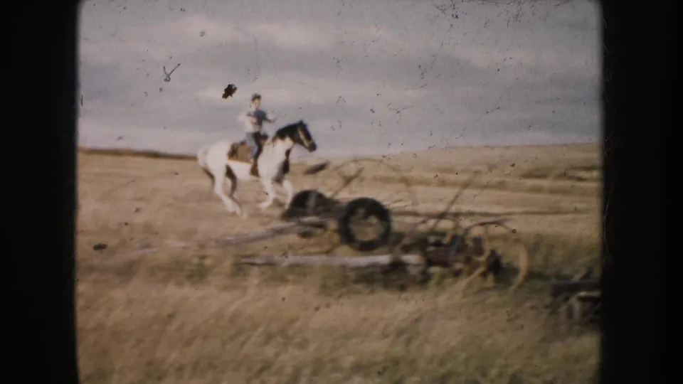 A rider on a black-and-white pinto horse passes old farm equipment in a South Dakota field, 1953.