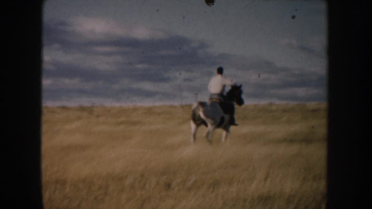 A distant rider on a pinto horse crosses South Dakota prairie beneath a broad, clouded sky in faded 8mm color.