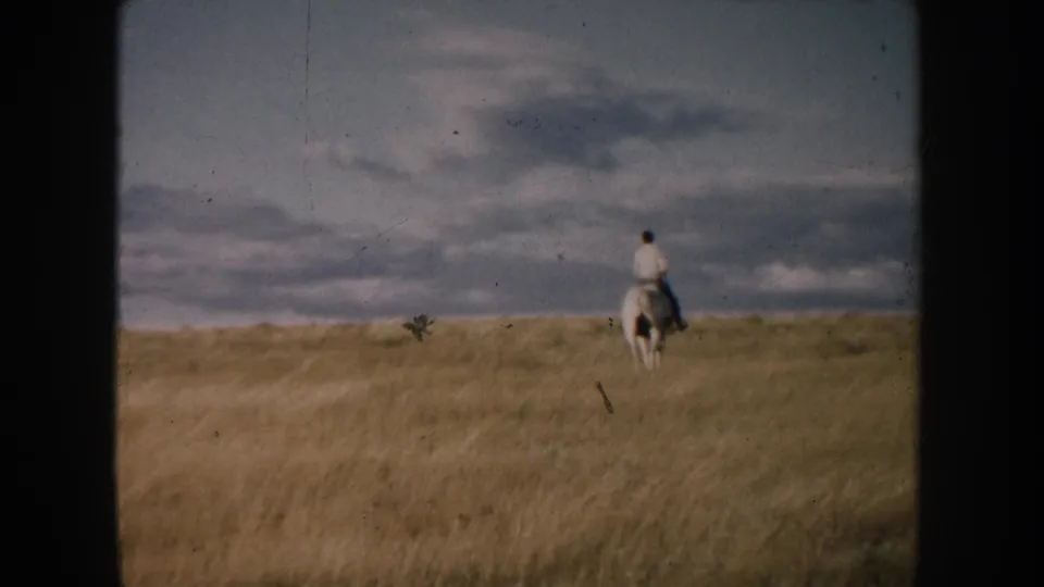 A small horseback rider nears the horizon line in a South Dakota prairie view, framed by dark 8mm film edges.