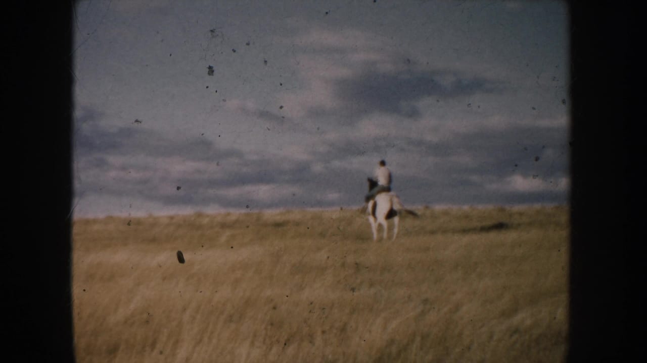 A distant horseback rider in South Dakota appears near the right side of the frame, moving across open prairie under layered clouds.