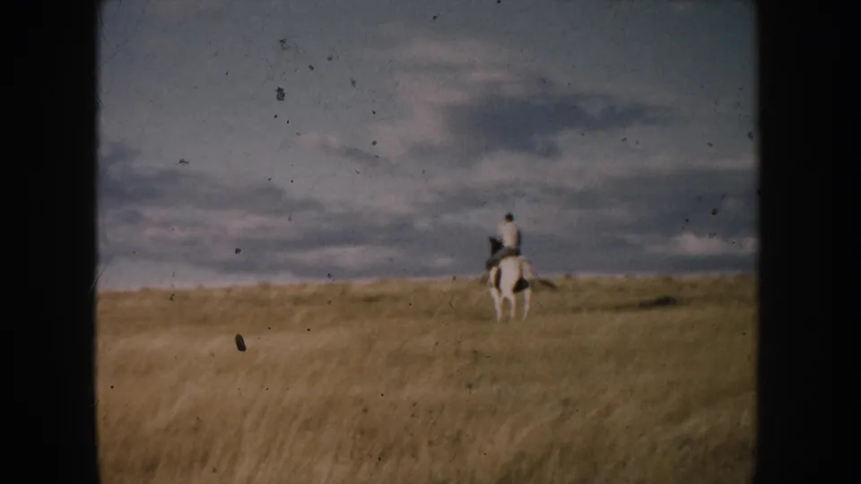 A distant horseback rider in South Dakota appears near the right side of the frame, moving across open prairie under layered clouds.
