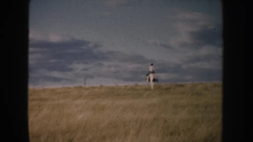 1953 South Dakota 8mm frame showing a distant lone rider on horseback on open grassland under clouds.