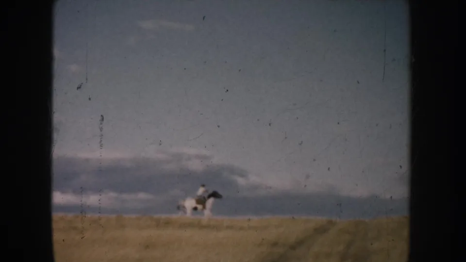Distant horseback rider on South Dakota prairie, seen through soft 8mm focus and visible film wear.