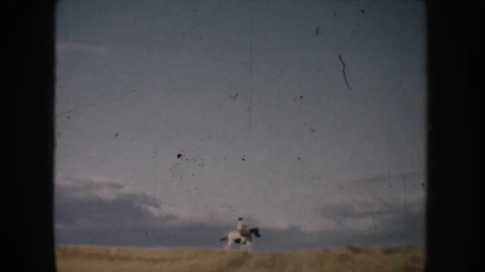 Wide 1953 home-movie view of a horse and rider crossing open South Dakota grassland beneath pale clouds.