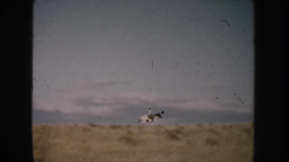 1953 South Dakota 8mm frame with a distant rider on horseback crossing open sandy grassland beneath a clouded sky.