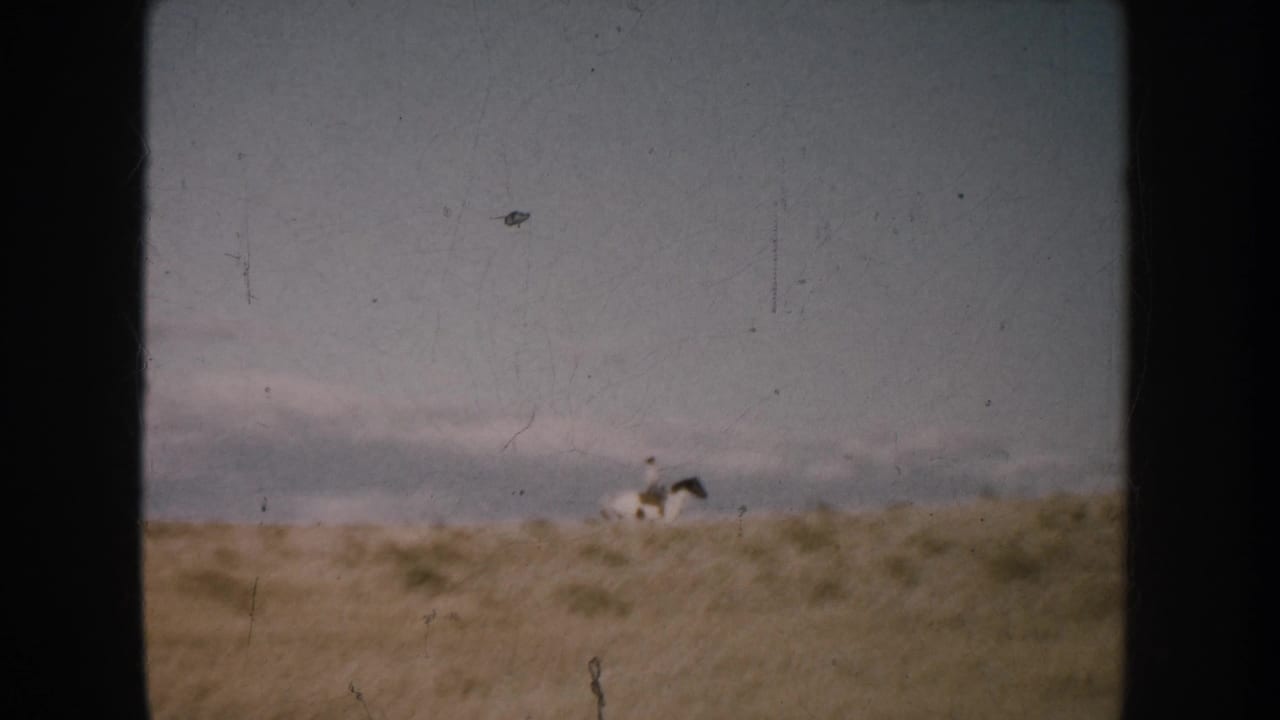 Distant horseback rider in a South Dakota open landscape, seen through a worn 8mm frame with sky and low grassland.
