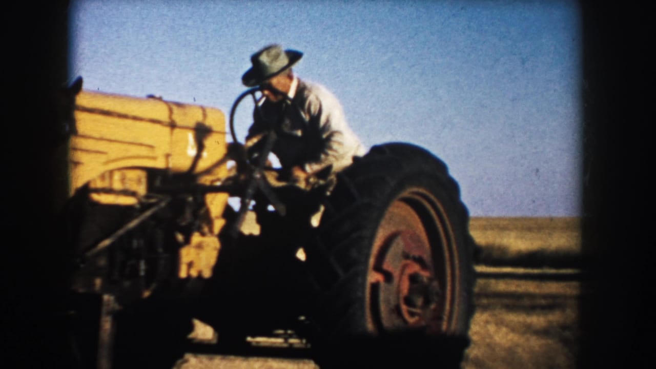 In 1953 South Dakota footage, a farmer in a light shirt and brimmed hat climbs onto a yellow tractor under a clear sky.
