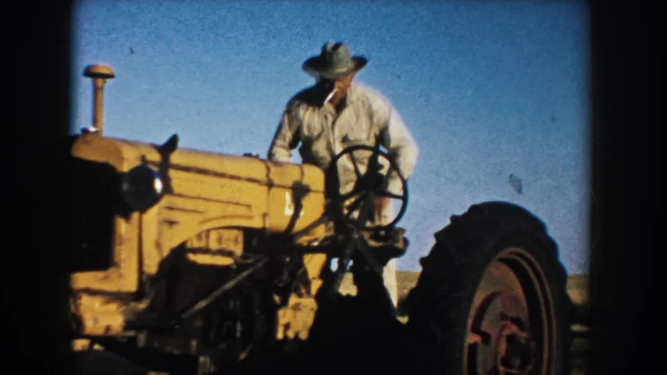A farmer sits at the steering wheel of a yellow tractor in an open South Dakota field, consistent with the 1953 clip metadata.