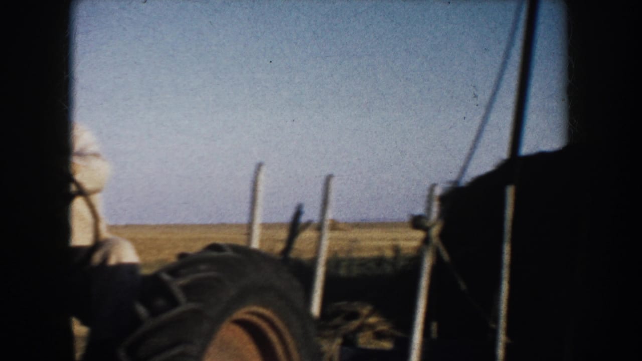 Farmer on a tractor beside hay bales in an open field.
