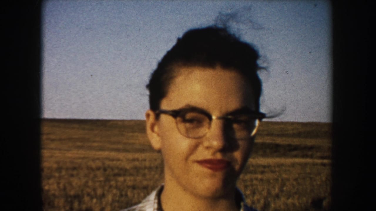 Young woman with glasses faces the camera in a South Dakota field, consistent with the supplied 1953 farm home-movie metadata.