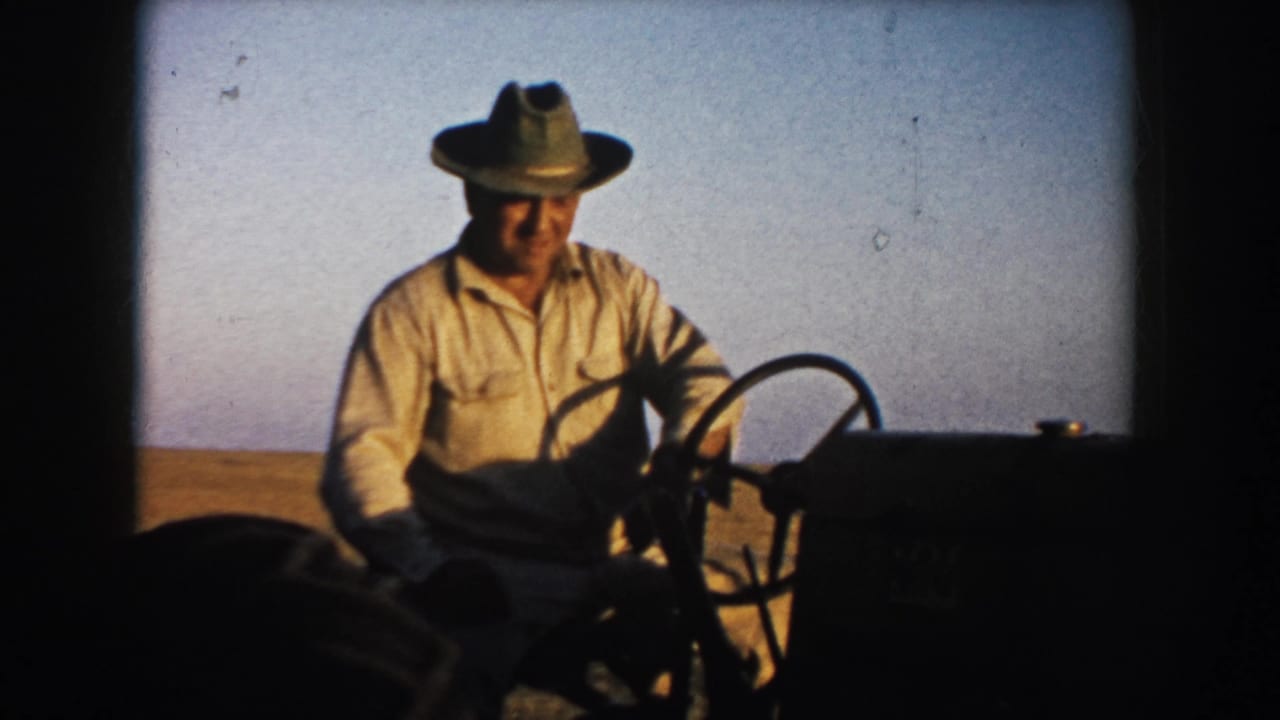 Close view of a 1953 South Dakota farmer operating a tractor, with broad field and clear sky in the background.