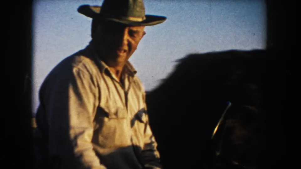 The farmer on the tractor moves near the camera, with his face, hat and shirt visible against the South Dakota field setting.