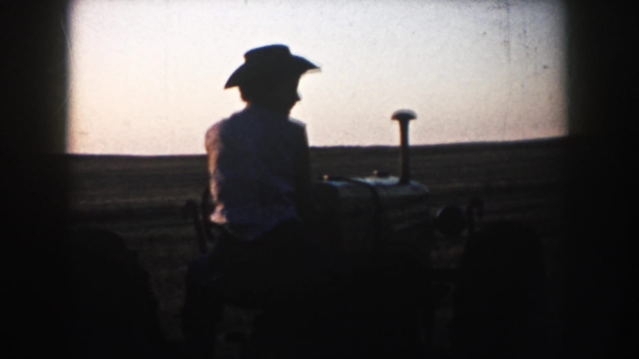 Silhouetted tractor operator in a cowboy hat against dusk farmland.