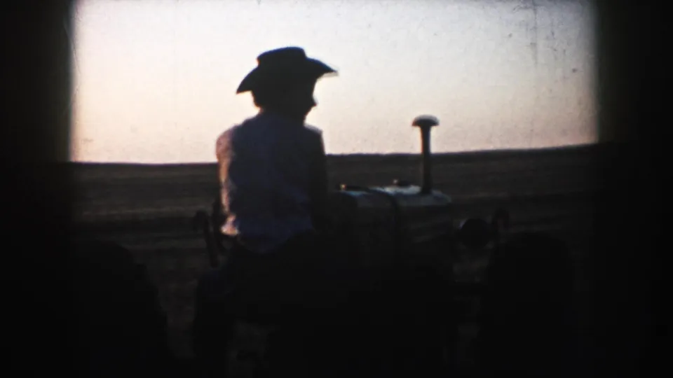 1953 South Dakota 8mm frame showing a silhouetted tractor operator in a cowboy hat beside open farmland at dusk.