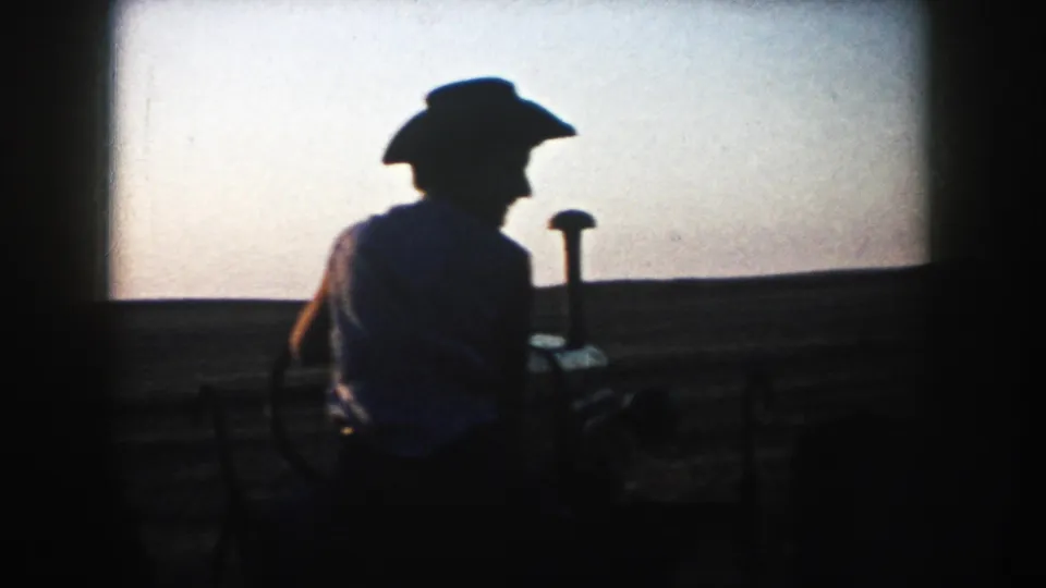A silhouetted tractor operator appears in profile on South Dakota farmland, with the horizon and dusk sky behind.