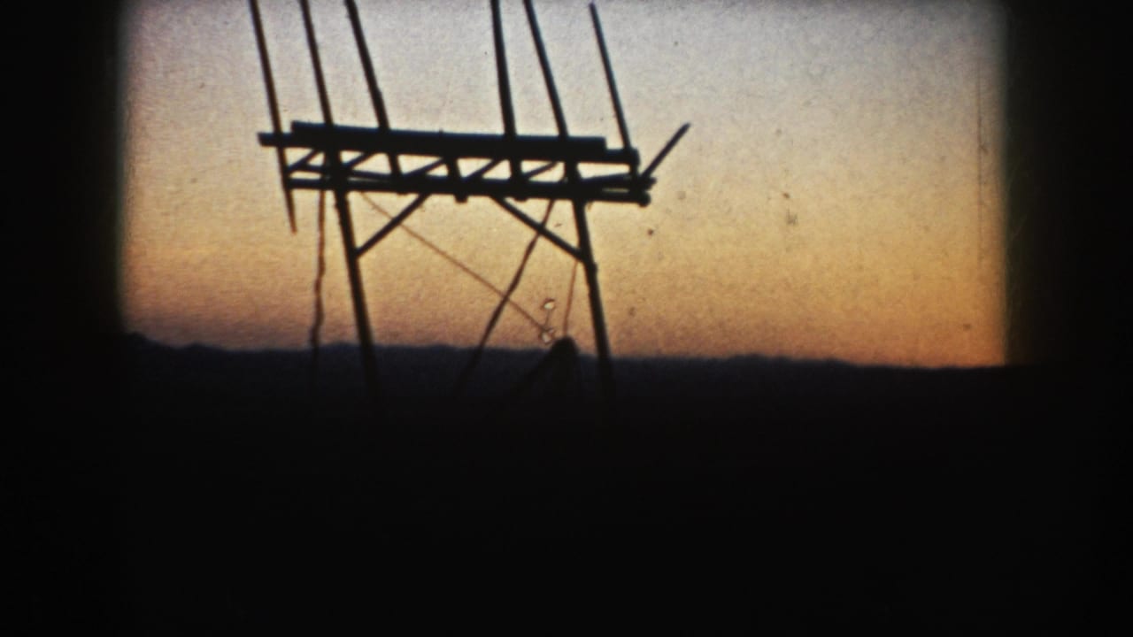A wooden farm structure, possibly an agricultural frame or bin support, is silhouetted against the South Dakota evening sky.