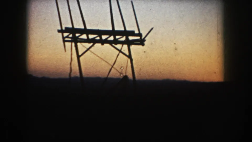A wooden farm structure, possibly an agricultural frame or bin support, is silhouetted against the South Dakota evening sky.