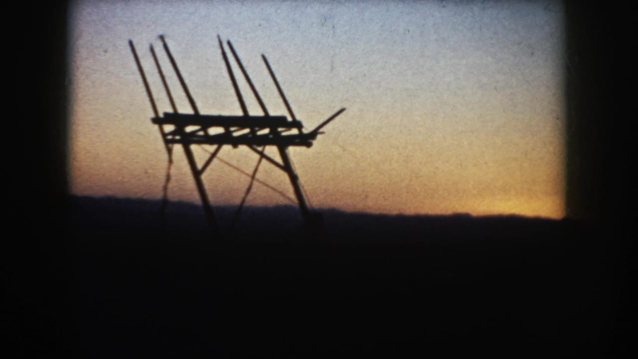 Silhouetted wooden farm structure against a sunset sky and dark horizon.