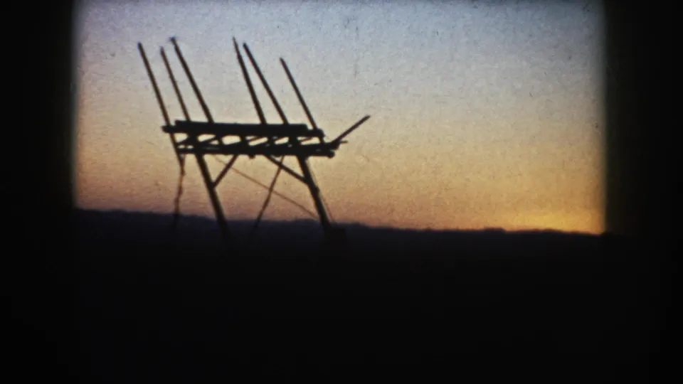 1953 South Dakota 8mm frame showing a silhouetted wooden farm structure against a warm sunset sky and low dark horizon.