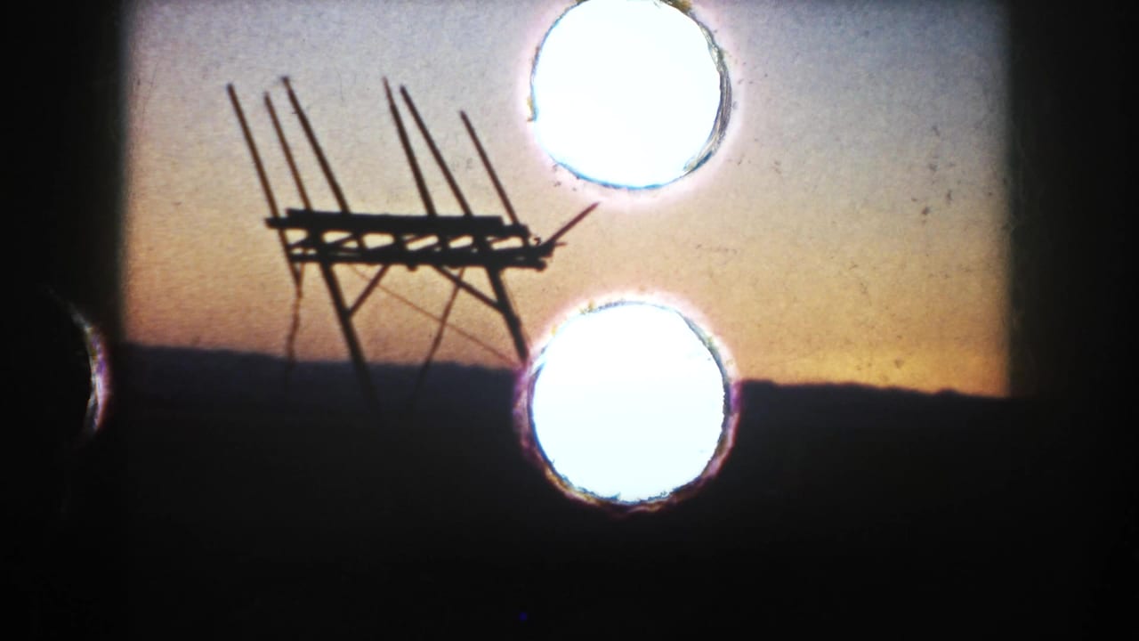 1953 South Dakota 8mm frame with a silhouetted farm structure, sunset horizon, and bright circular film artifacts near the right side.
