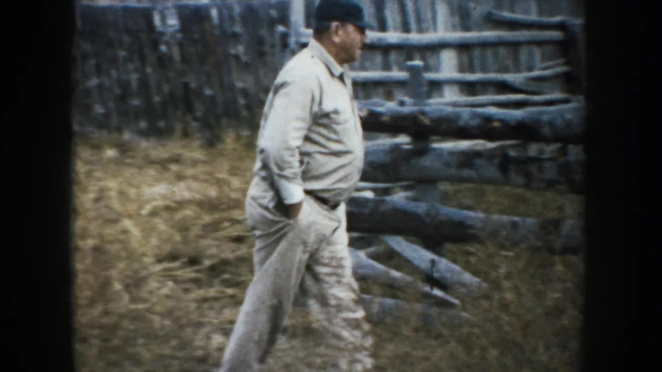 A farmer in light work clothes walks past rough rail fencing on the 1953 South Dakota farm.