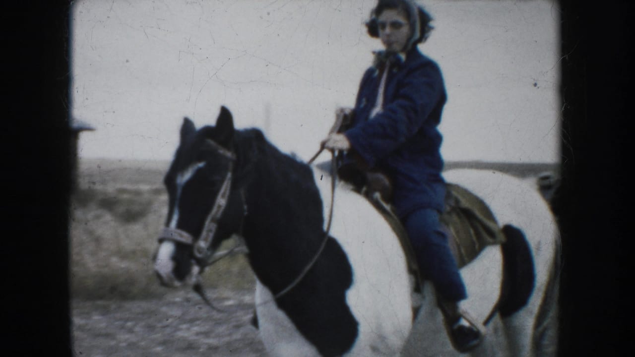 A woman wearing a blue coat and scarf rides a black-and-white pinto horse toward the camera in a 1953 South Dakota home movie.