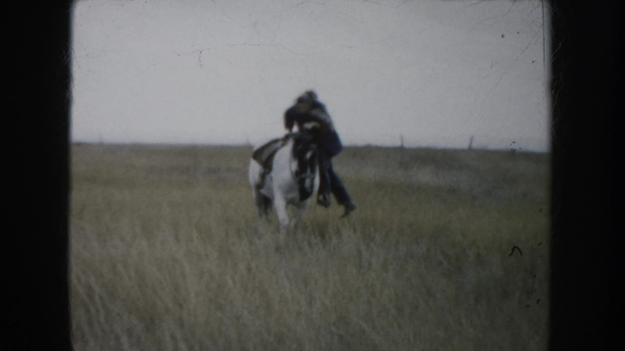 1953 South Dakota ranch footage frame with a distant rider on a white and dark horse crossing tall pasture grass.