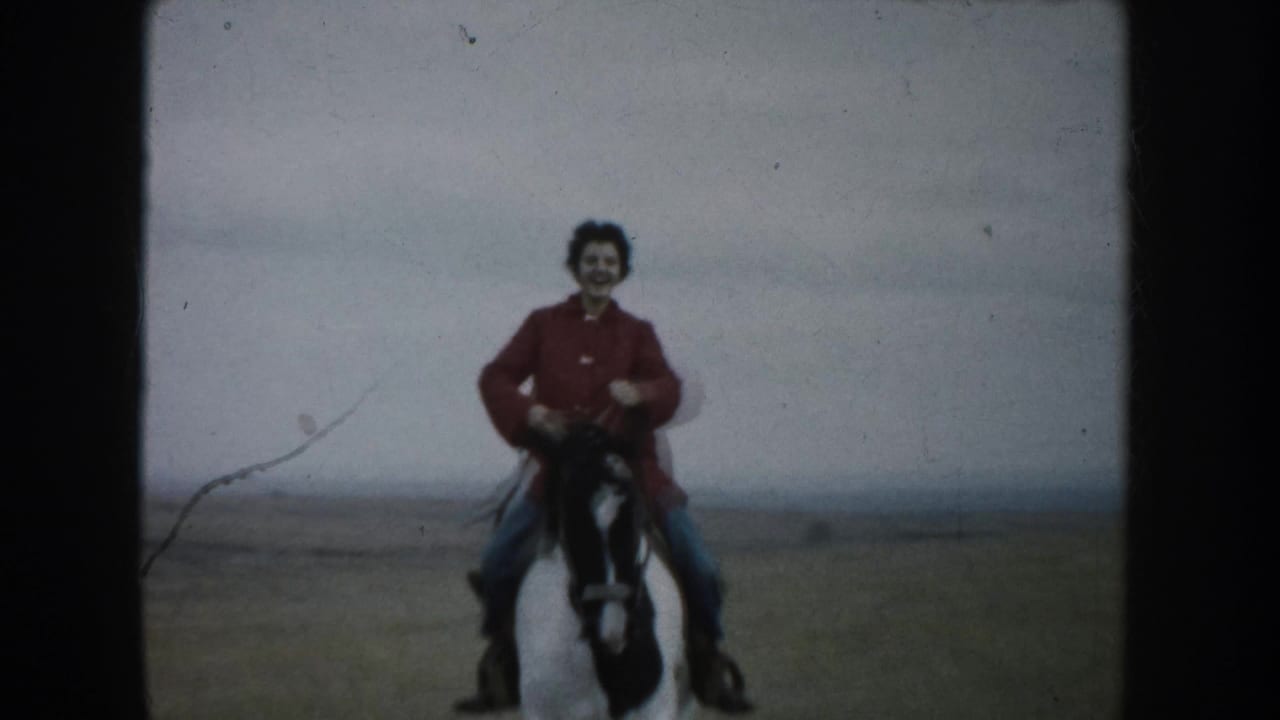 Young rider in a red jacket approaches on a horse across open prairie.