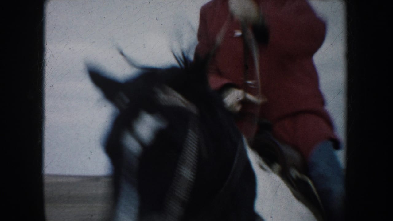The rider in a red jacket passes close to the camera on a dark-maned horse in the South Dakota prairie scene.