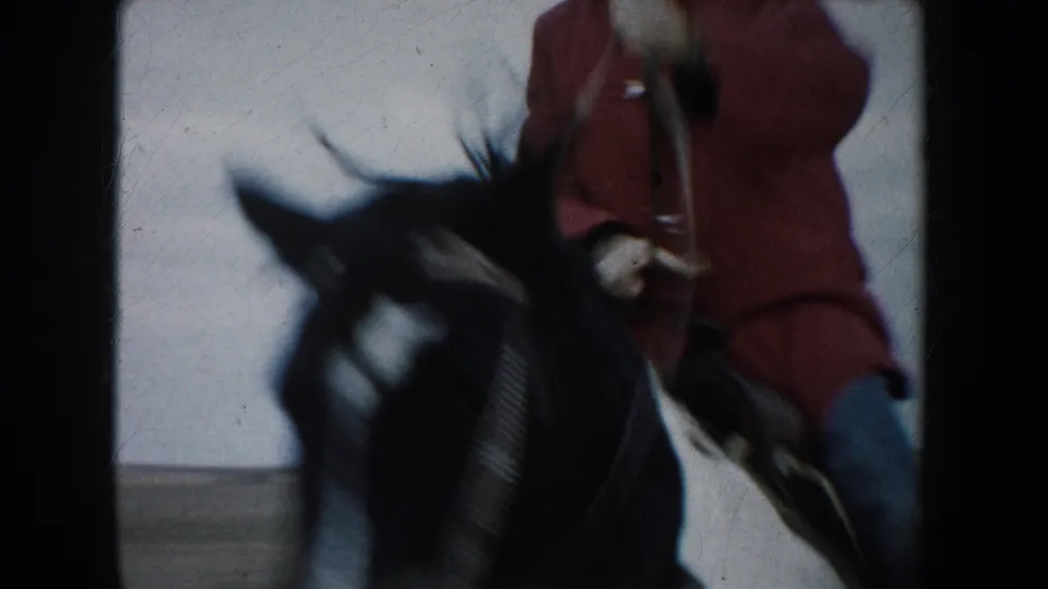 The rider in a red jacket passes close to the camera on a dark-maned horse in the South Dakota prairie scene.