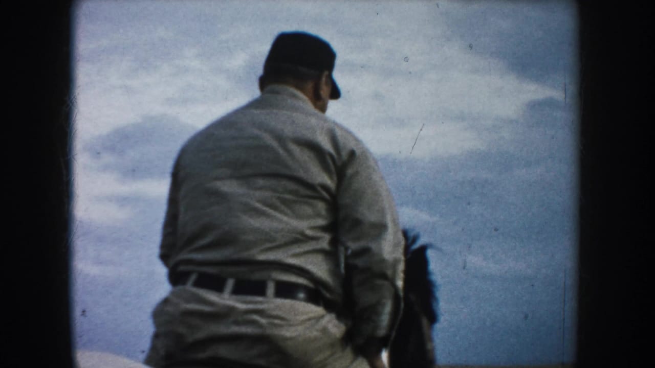 An older male rider in a light shirt and dark cap is viewed from behind on horseback in the 1953 South Dakota footage.