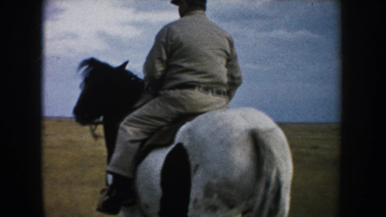 An older rider in light clothing rides away on a white horse with dark markings across open South Dakota prairie.