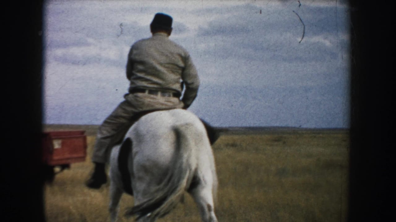 Rear view of an adult rider on a brown-and-white horse in South Dakota grassland, with a red pickup visible at left.