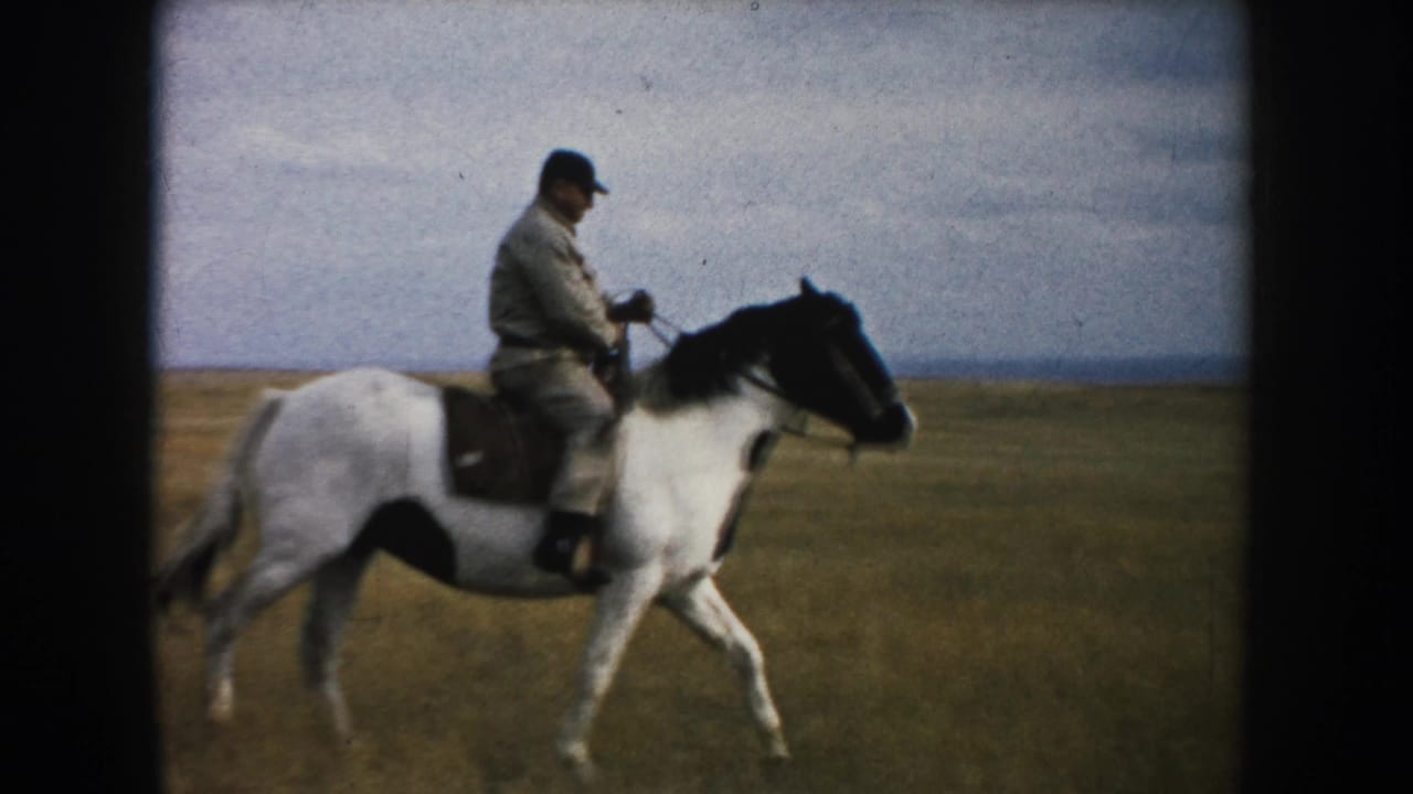 Side view of an adult man riding a brown-and-white horse across open South Dakota grassland in 1953 8mm footage.
