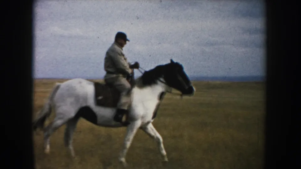 Side view of an adult man riding a brown-and-white horse across open South Dakota grassland in 1953 8mm footage.