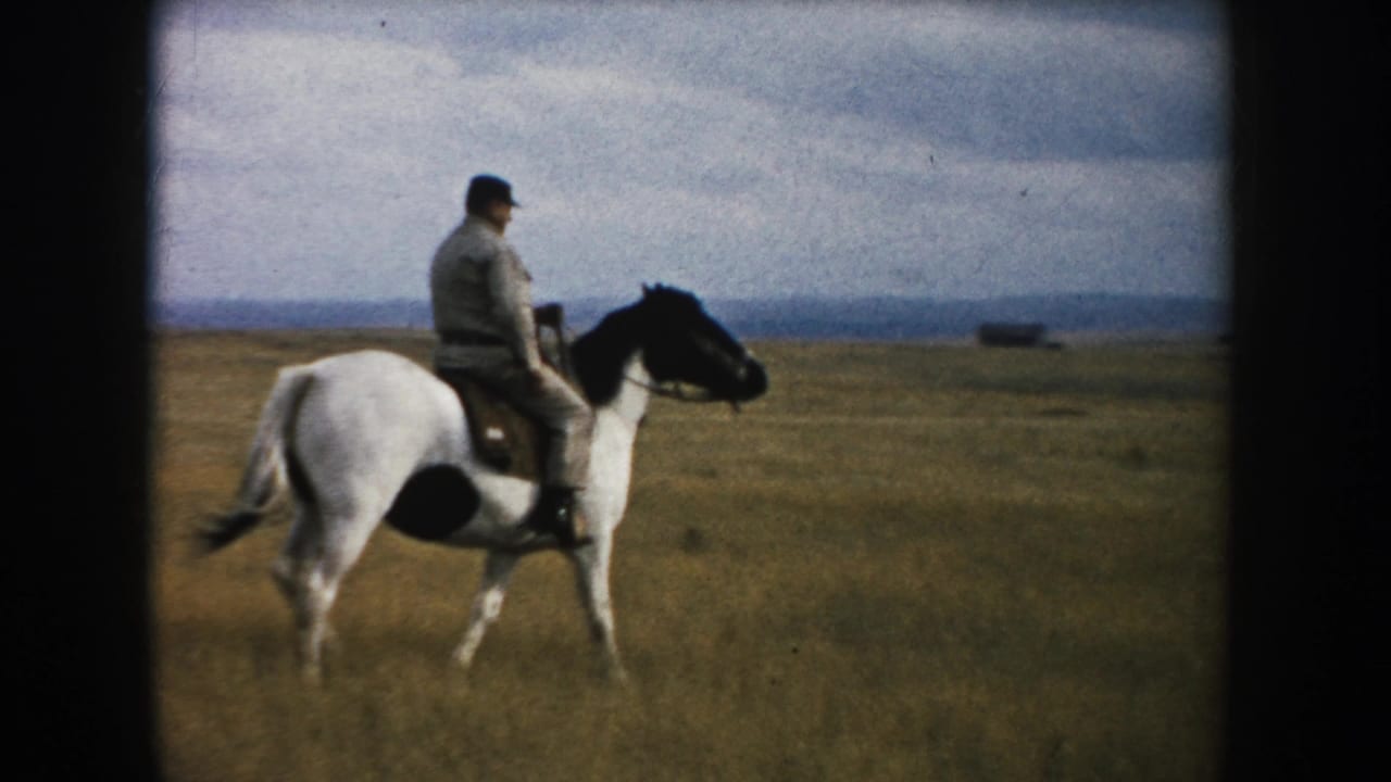 The 1953 South Dakota home-movie frame shows the rider and black-and-white horse moving across open grassland.