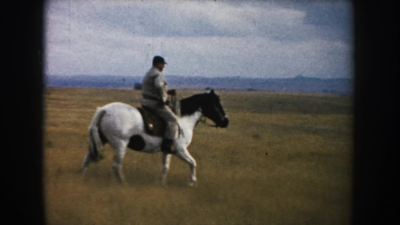 Side view of an adult rider on a black-and-white horse in South Dakota prairie footage dated 1953 by metadata.