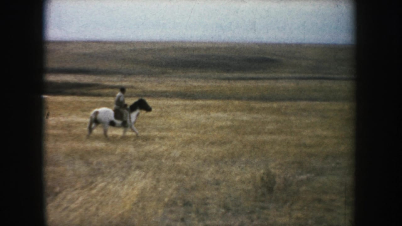 A wider 1953 South Dakota frame places the horseback rider small within a broad, open prairie field.