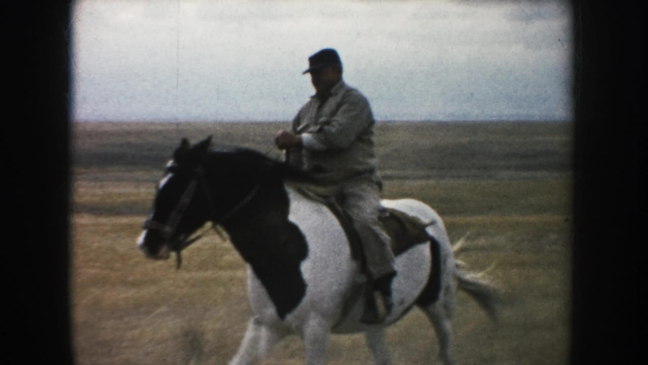 1953 South Dakota frame showing a closer side view of the man riding a pinto horse in open grassland.
