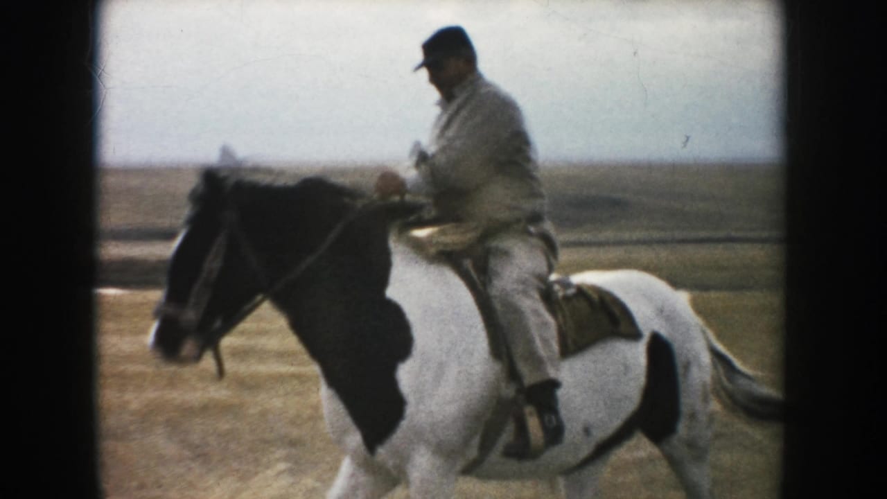 1953 South Dakota 8mm frame showing an adult rider on a black-and-white pinto horse moving past the camera on open prairie.