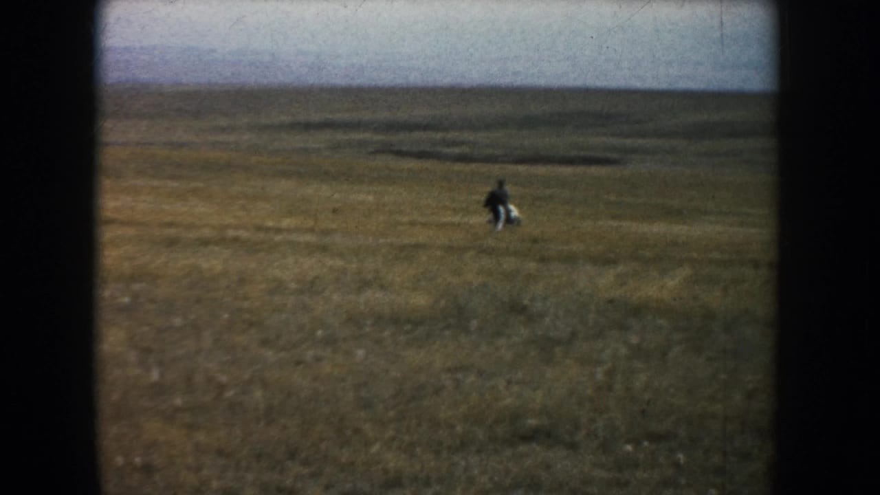 Wide 1953 South Dakota prairie view with a distant adult rider on horseback in an open grassland landscape.