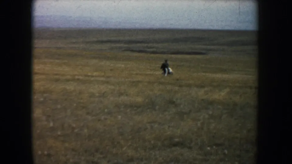 Wide 1953 South Dakota prairie view with a distant adult rider on horseback in an open grassland landscape.