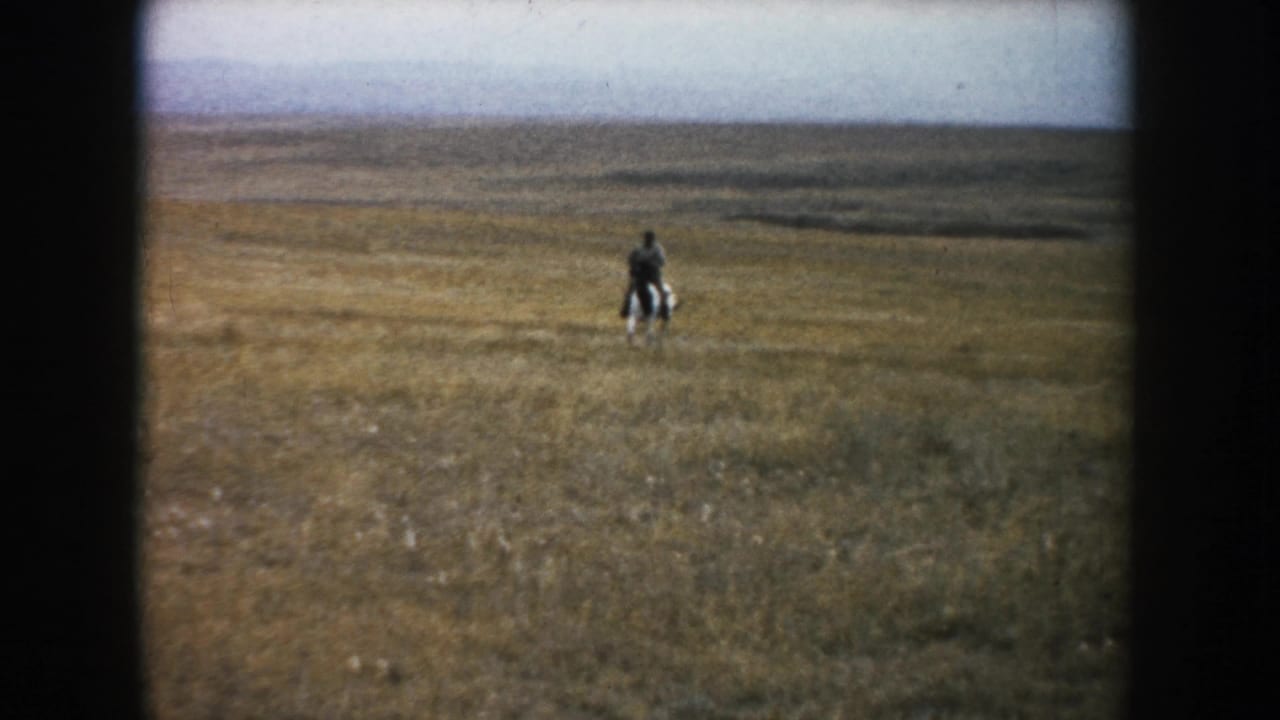 In supported 1953 South Dakota footage, a distant adult rider moves across dry open prairie beneath a broad cloudy sky.